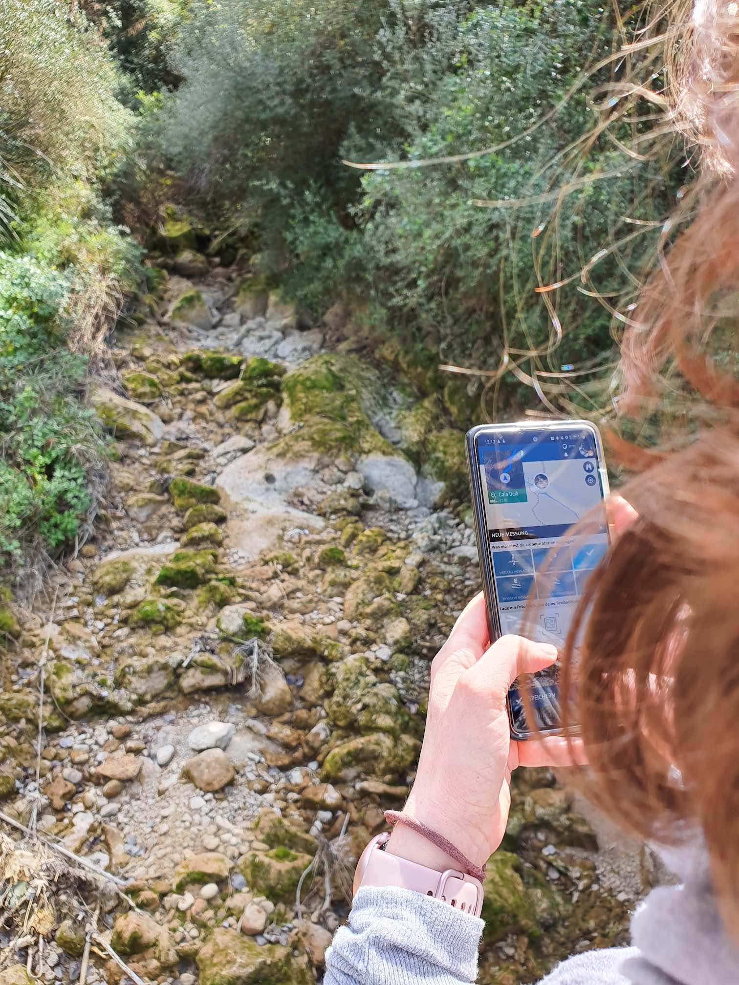 a person holding a mobile phone against a stream