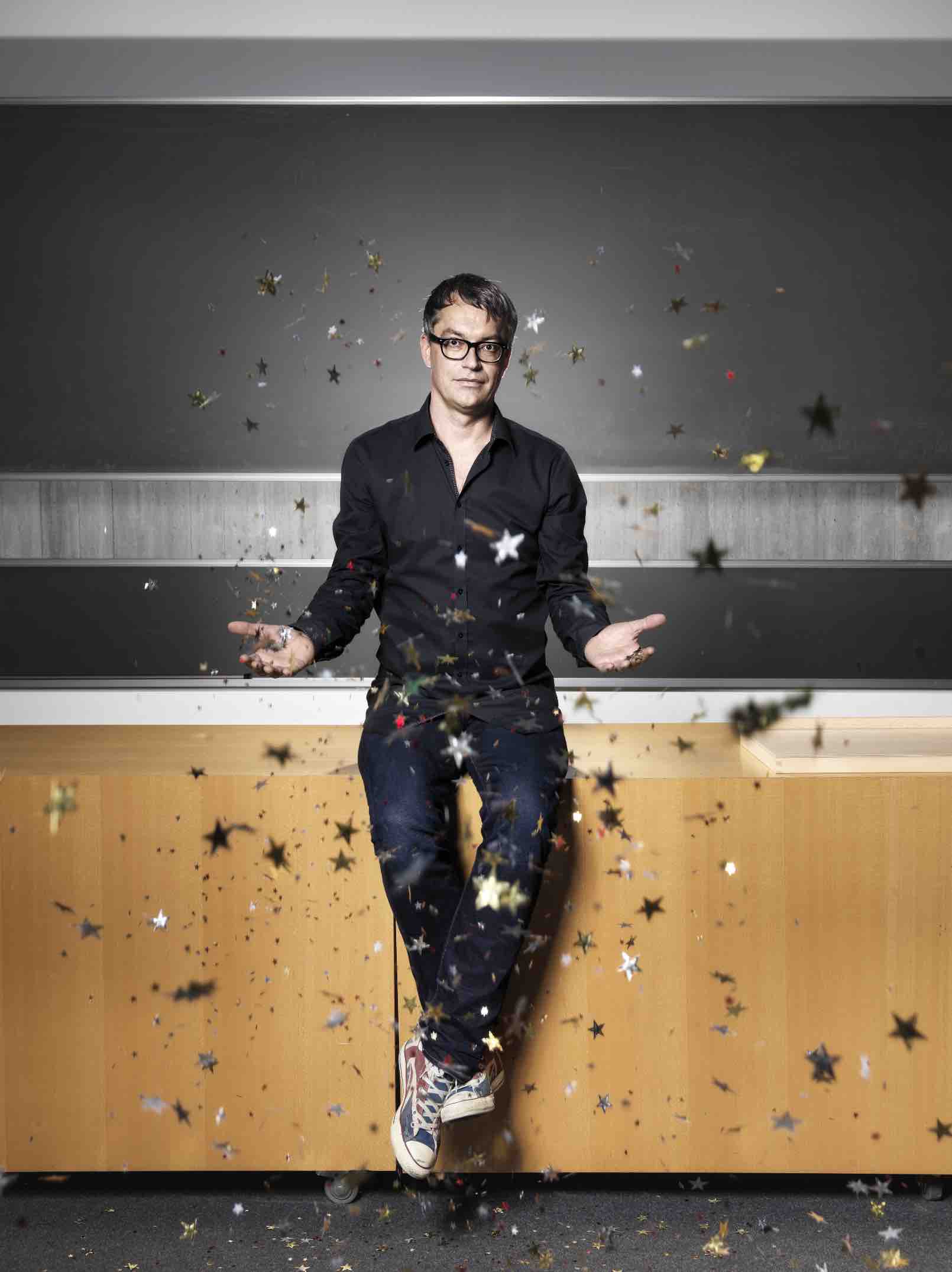 A scientist (Ben Moore) sits in front of the lecture room surrounded by star-shaped confetti