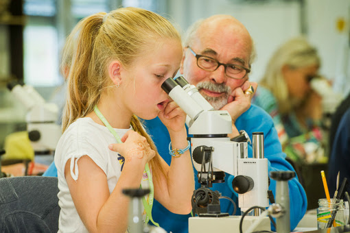 a girl at a microscope and an old man beside her 